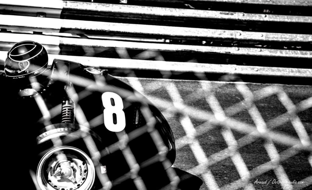 Entre deux mondes : le regard est invité à traverser le flou d'un grillage pour découvrir l'intimité du cockpit de Jim Clark. Un noir et blanc intemporel qui transforme la course automobile en une scène suspendue, presque silencieuse