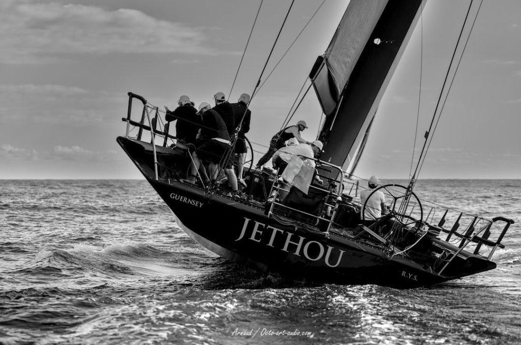 Photographie artistique en noir et blanc du voilier de course Jethou gîtant fortement, équipage en action, lors d'une régate de prestige à Saint-Tropez.
