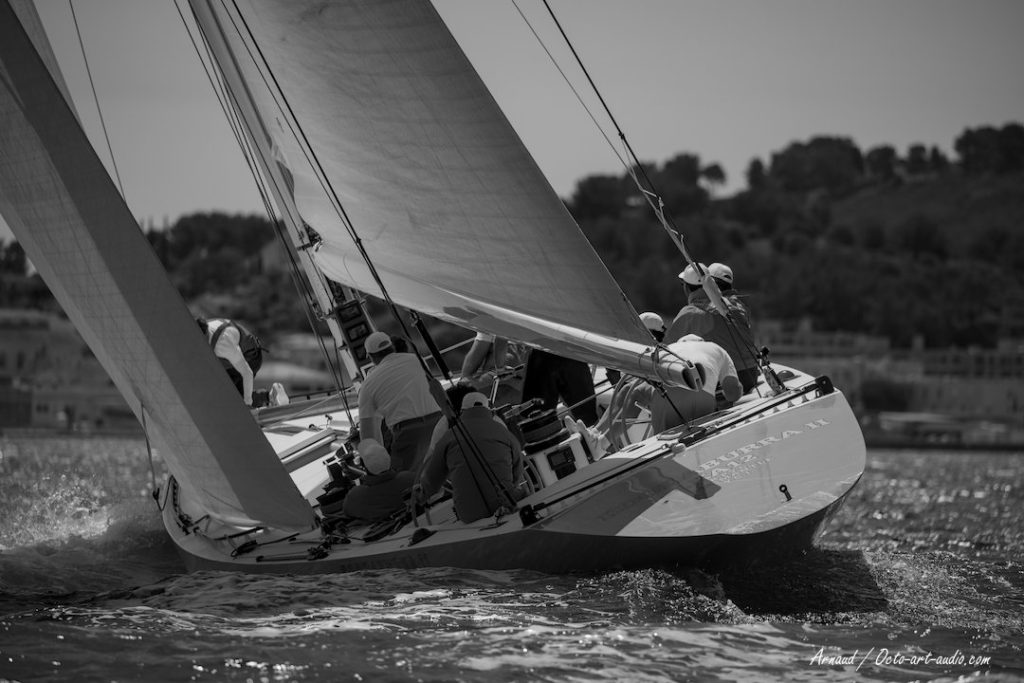 Photographie en noir et blanc du 12mJI Kookaburra II (KA-12) en pleine gîte lors de la Toulon Provence Regatta 2026, vue sur le tableau arrière et l'équipage.