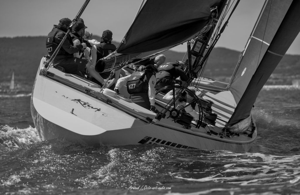 Vue rapprochée du tableau arrière du 12mJI Kiwi Magic (KZ-7) en pleine régate à Toulon, équipage en action et gîte marquée.