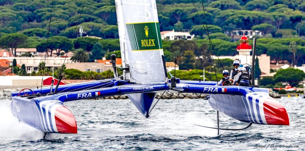 Photographie du catamaran volant F50 de l'équipe de France SailGP en pleine vitesse devant le phare de Saint-Tropez.