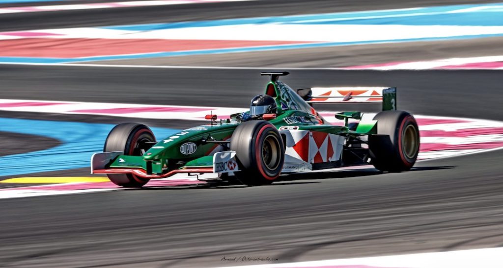 Photographie en filé dynamique de la F1 Jaguar Racing (British Racing Green) avec les sponsors HSBC, en course sur le circuit Paul Ricard, avec les bandes de dégagement bleues et rouges.