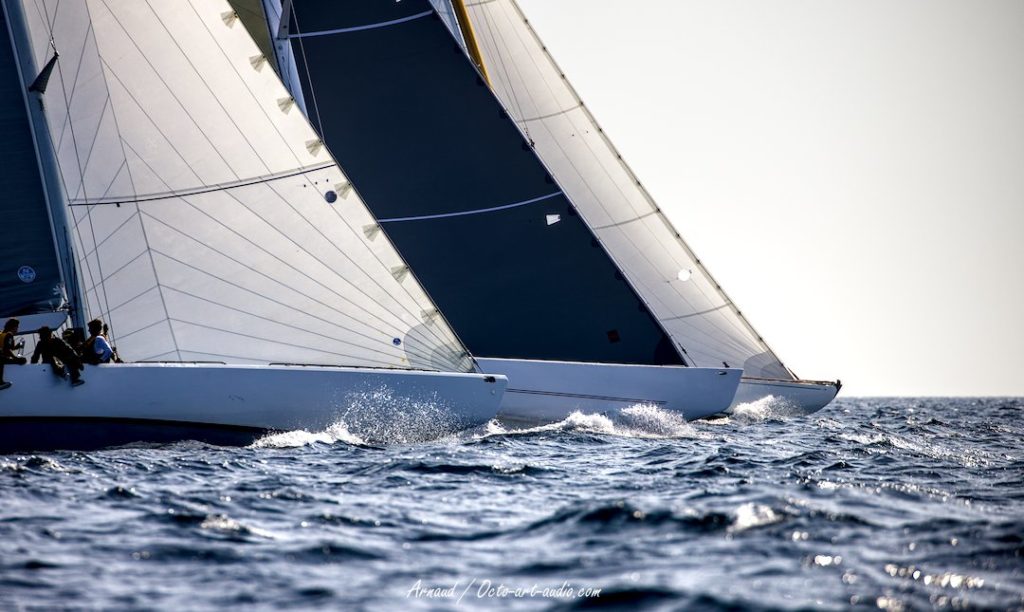 Trois voiliers de la classe 12mJI en régate serrée, montrant la puissance de leurs étraves et le contraste de leurs voiles modernes et classiques.