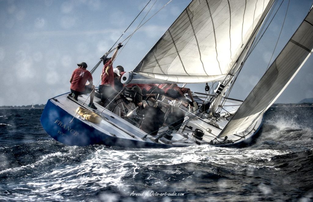 Le 12mJI France 3 (F-8) en pleine action lors de l'Europa Cup à Hyères, vue dynamique de l'équipage et de la coque bleue.