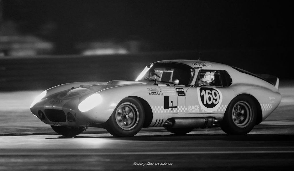 Photographie d'art en noir et blanc d'une Shelby Cobra Daytona Coupé (numéro 169) en pleine course nocturne, filé parfait montrant la vitesse.