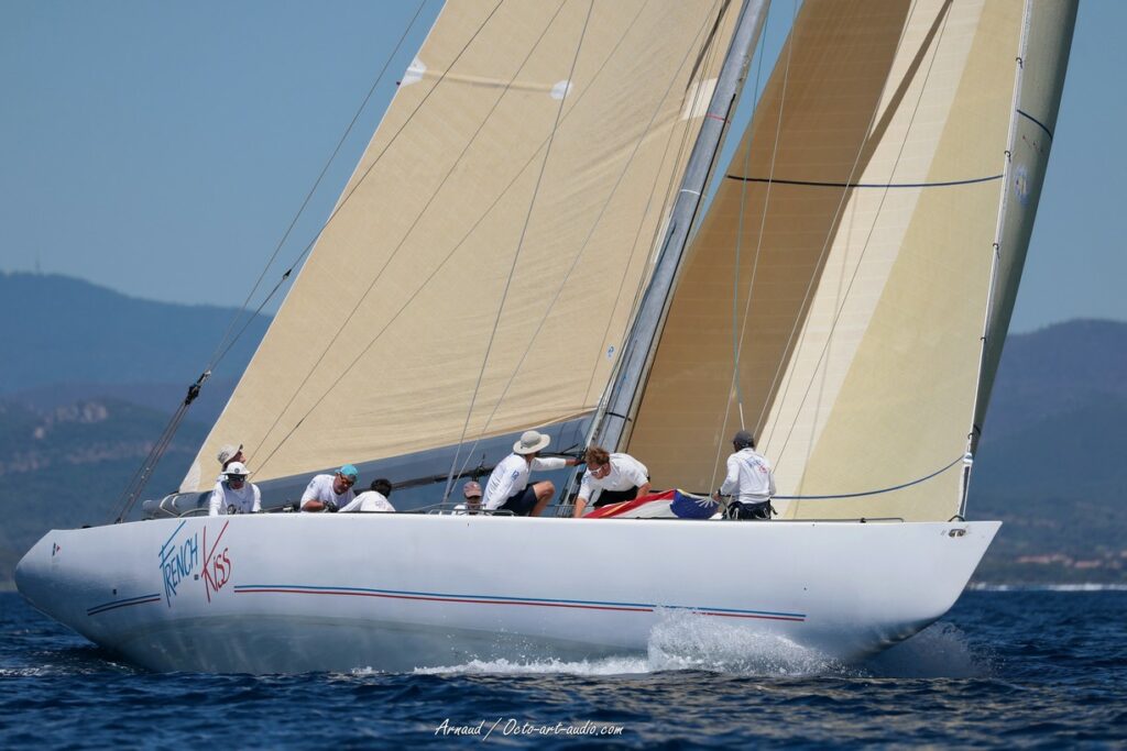 Photographie de trois-quarts arrière du voilier classique 12mJI French Kiss F-12 naviguant sous voiles ambrées avec son équipage lors de l'Europa Cup 2026 à Hyères.