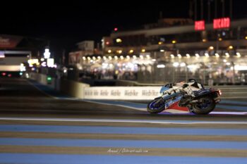 Session de nuit magique au Bol d'Or Classic : la Suzuki affronte la piste du Castellet sous les projecteurs. Course de nuit au Bol d'Or Classic sur le Circuit Paul Ricard avec une moto Suzuki en pleine accélération devant les stands illuminés.