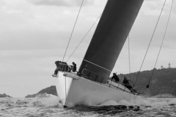 La force des éléments : Un MAXI voilier gîte sous la puissance du vent lors des Régates de Saint Tropez Photographie en noir et blanc d'un grand voilier classique MAXI type gîté par gros temps, vagues déferlantes contre l'étrave, équipage visible au rappel sur le pont, lors des Régates LES VOILES DE SAINT TROPEZ.