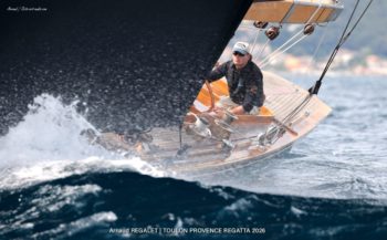 Flica II (K-14) : Puissance et élégance sur les eaux de Toulon. Le 12mR Flica II en pleine gîte avec gros plan sur le pont en bois et le barreur, Toulon Provence Regatta 2026.