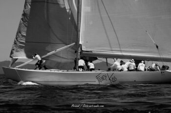 L'esprit d'équipe à bord de French Kiss. L'équipage du célèbre 12mJI s'active au rappel et aux manœuvres sous la grand-voile lors de l'Europa Cup 2026. Tirage d'art disponible en édition limitée. Photographie d'art en noir et blanc de profil du voilier classique 12mJI French Kiss F-12, mettant en valeur son nom sur la coque et son équipage en action lors de l'Europa Cup 2026 à Hyères.