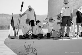 Marc Pajot et son équipage à bord de French Kiss. Le célèbre skipper français mène ses hommes lors des régates de l'Europa Cup 2026, quarante ans après l'épopée de Fremantle. Tirage d'art disponible en édition limitée. Photographie d'art en noir et blanc du skipper Marc Pajot et de son équipage en pleine action à la poupe du voilier classique 12mJI French Kiss lors de l'Europa Cup 2026 à Hyères.