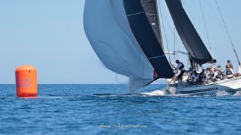 Manœuvre millimétrée à la bouée. Le légendaire 12mJI en composite New Zealand (KZ-7), le célèbre "Plastic Fantastic", négocie sa marque de parcours lors de l'Europa Cup 2026. Tirage d'art disponible en édition limitée. Photographie du voilier classique 12mJI New Zealand KZ-7, surnommé Plastic Fantastic, manœuvrant son spinnaker à côté d'une bouée orange Toulon Provence Méditerranée lors de l'Europa Cup 2026 à Hyères.