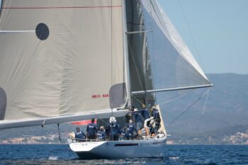 Coordination et puissance. L'équipage du 12mJI South Australia (KA-8) en plein réglage sous la grand-voile lors des épreuves de l'Europa Cup 2026. Tirage d'art disponible en édition limitée. Photographie de trois-quarts arrière du voilier de tradition 12mJI South Australia KA-8, montrant l'équipage en action sur le pont lors des régates de l'Europa Cup 2026 à Hyères.