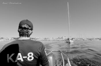 Les coulisses de l'Europa Cup. Remorquage matinal du 12mJI South Australia (KA-8) lors de la sortie du port de Hyères, avant l'envoi des toiles. Tirage d'art disponible en édition limitée. Photographie d'art en noir et blanc montrant le remorquage du voilier classique 12mJI South Australia KA-8 par un bateau d'assistance lors de la sortie du port de Hyères pour l'Europa Cup 2026.