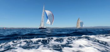 Envolée sous spi en baie de Hyères. Les mythiques 12mJI France 1 et South Australia (KA-8) ouvrent grand leurs voiles de portant lors de l'Europa Cup 2026. Tirage d'art disponible en édition limitée. Photographie marine prise depuis l'eau montrant les voiliers de tradition 12mJI France 1 et South Australia KA-8 sous spinnaker lors de l'Europa Cup 2026 à Hyères. Premier plan sur l'écume blanche des vagues.