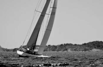 Puissance et contrastes. Les lignes tendues du 12mJI French Kiss (F-12) sculptant le plan d'eau hyérois lors de l'Europa Cup 2026. Tirage d'art disponible en édition limitée. Photographie d'art en noir et blanc du voilier classique 12mJI French Kiss F-12 en pleine gîte lors de l'Europa Cup 2026 à Hyères. Vue de trois-quarts arrière sur le cockpit et la voilure élancée frôlant les côtes du Var.