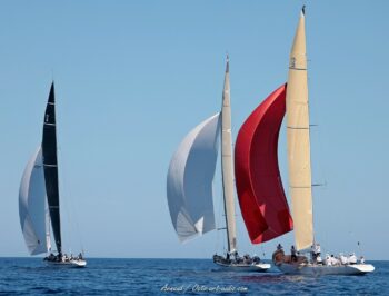 Confrontation de légendes dans la rade de Hyères. Les géants de la Coupe de l'America, dont France (F-7) et New Zealand (KZ-7), déploient leurs spinnakers lors de l'Europa Cup 2026. Une composition maritime disponible en tirage d'art limité. Photographie de course au large réunissant trois voiliers classiques 12mJI, dont le France F-7 avec son spinnaker rouge et le New Zealand KZ-7, navigant de front sous un ciel bleu lors de l'Europa Cup 2026 à Hyères.