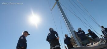 Force des lignes et bleu azur. L'équipage du South Australia face au soleil hyérois durant l'Europa Cup 12mJI 2026. Photographie d'art disponible en tirage limité. Photographie en contre-jour de l'équipage du voilier classique 12mJI South Australia KA-8 sous un ciel bleu azur intense, lors des régates de l'Europa Cup 2026 à Hyères. Gros plan en contre-plongée sur le mât et les marins en action.