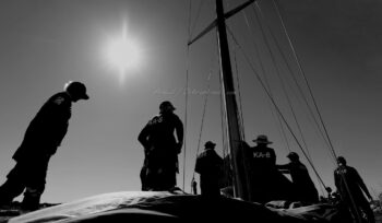 Tension et graphisme à la manœuvre à bord du 12mJI South Australia (KA-8). Instants capturés dans l'éclat des contre-jours hyérois lors de l'Europa Cup 2026. Tirage d'art en édition limitée. Photographie artistique en noir et blanc de l'équipage du voilier de tradition 12mJI South Australia KA-8, en contre-jour sous un soleil radieux lors de l'Europa Cup à Hyères. Composition graphique centrée sur le mât, les cordages et les silhouettes des équipiers à la manœuvre.