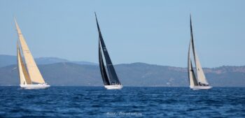 Parade de légendes en rade de Hyères. Les mythiques 12mJI French Kiss, New Zealand ("Plastic Fantastic") et South Australia alignent leurs carènes sous le soleil varois lors de l'Europa Cup 2026. Tirage d'art disponible en édition limitée. Photographie panoramique de trois voiliers classiques 12mJI dont French Kiss F-12, New Zealand KZ-7 et South Australia KA-8 naviguant de profil lors de l'Europa Cup 2026 à Hyères.